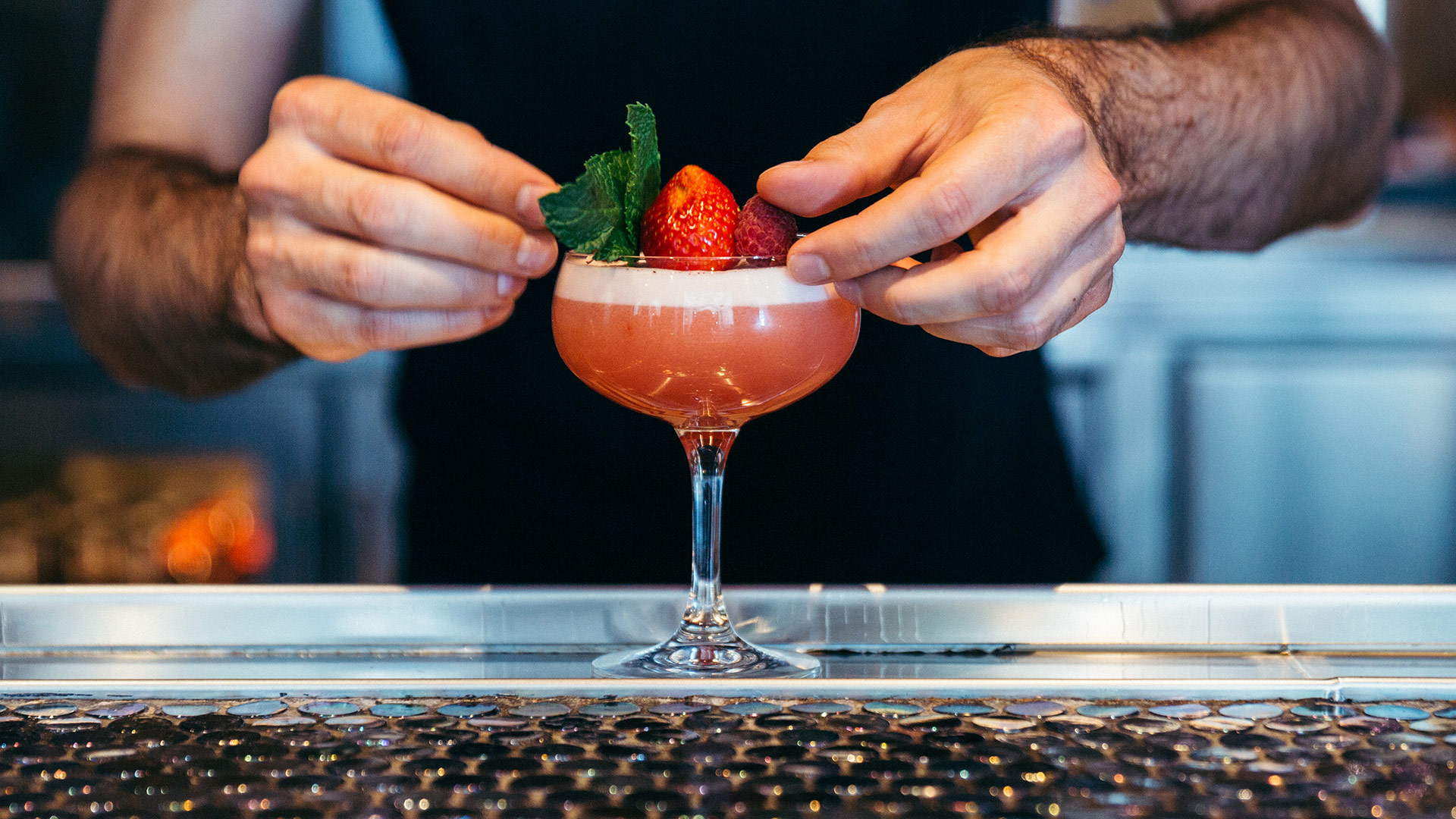 Hands finishing a cocktail with mint and berries